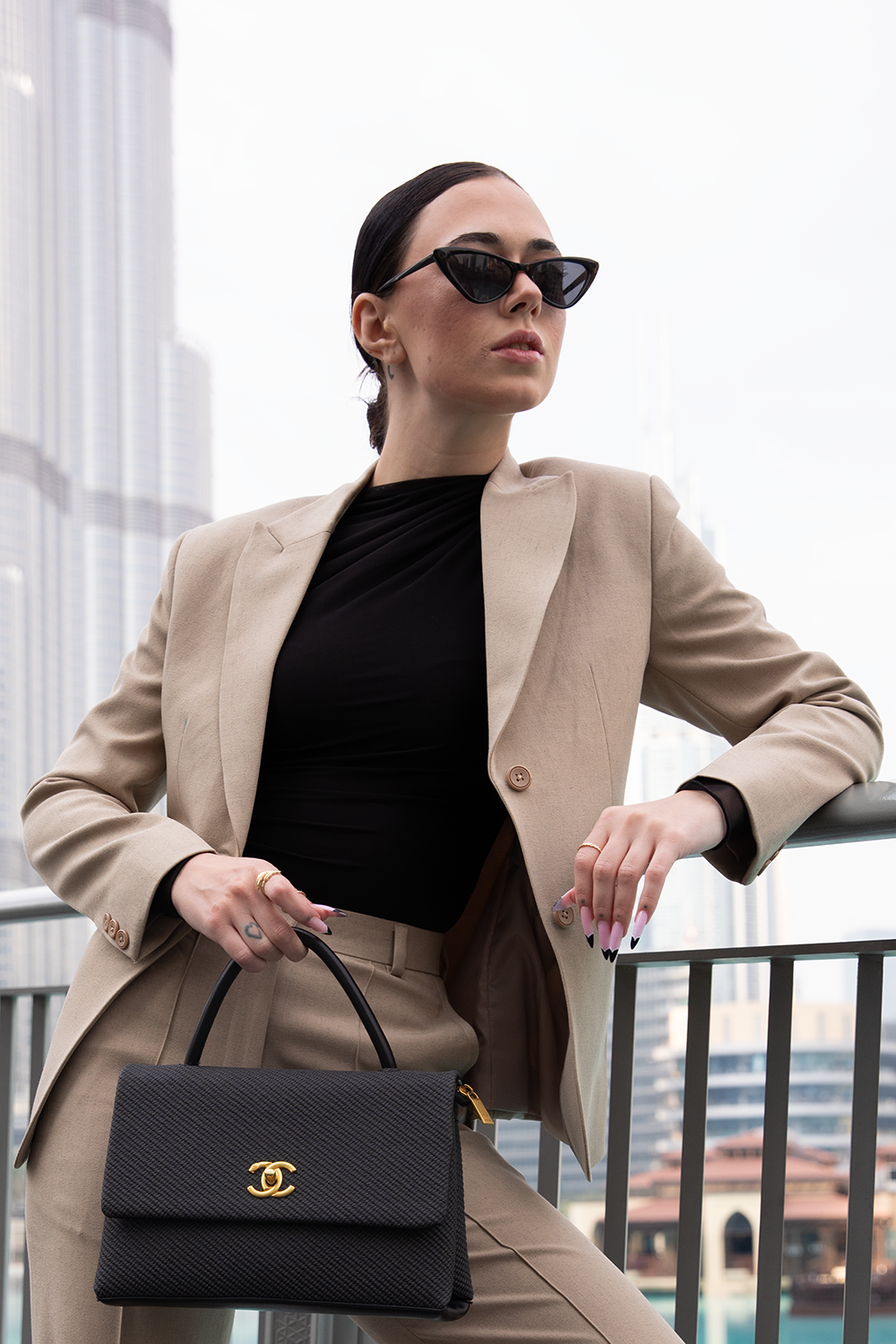 Woman in a beige suit holding a black handbag with a cityscape background